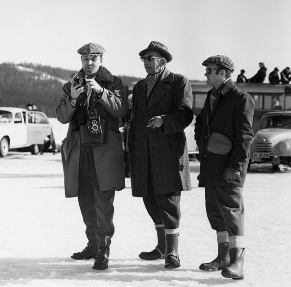 Tre män beskådar biltävling på Baksjön, i bakgr...