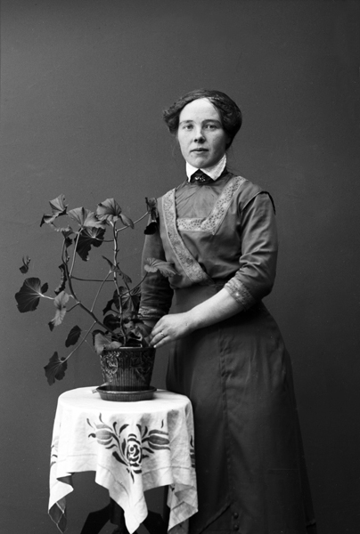 Ateljéfoto av en okänd kvinna vid ett pelarbord.