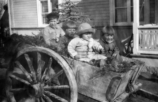 Fyra barn i en dyngkärra vid gården yst i backen.