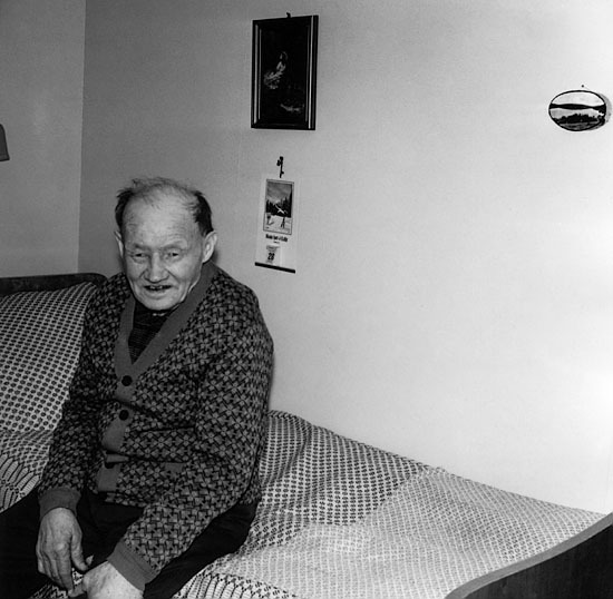 Bild av en okänd  äldre man på sängkanten.