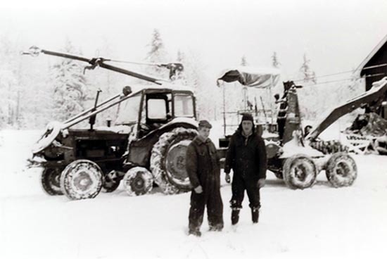 Två okända män framför en traktor med grävaggre...