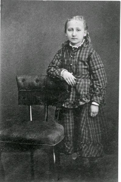 En okänd flicka står vid en stol.