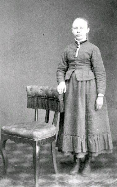 En okänd flicka står vid en stol.