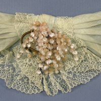 SLM 22058 - Klänningsdekoration, rosett av linne och spets, dekorerad med en kvist av rosa mimosa