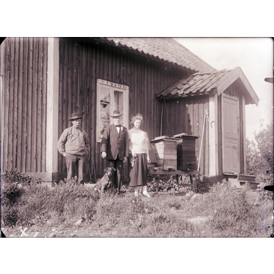 SLM X1913-78 - Tre personer och en hund framför ett hus.