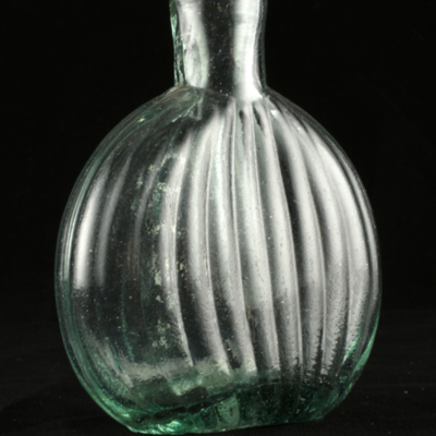 SLM 2437 - Liten flaska av grönt glas, platt och rund, ribbad sida, från Flens socken