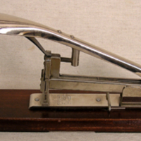 SLM 32620 - Häftapparat av polerat stål på en fyrkantig platta av vinrödmålat trä