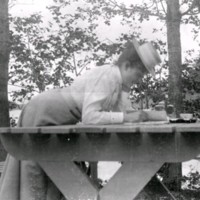 SLM M034122 - En kvinna lutar sig över ett bord läsande något.
