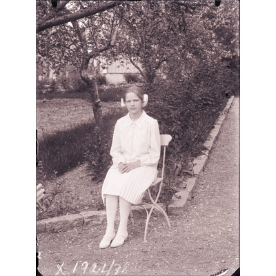SLM X1921-78 - Finklädd flicka sittandes på en stol i en trädgård