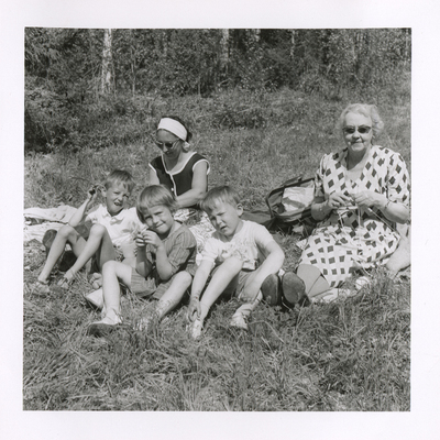 SLM P2018-0328 - Brita och barnen sitter på en filt i gröngräset med svärmor, 1950-tal.