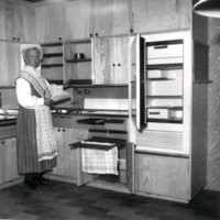 SLM M033866 - Kvinna iklädd sockendräkt demonstrerar ett kök.