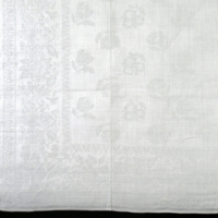 SLM 5414 - Servett av vit linnedamast med blomstermotiv, märkt 