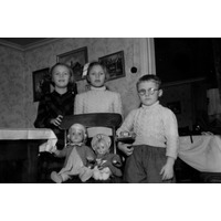 002060 - Tre barn står vid en stol med dockor på.