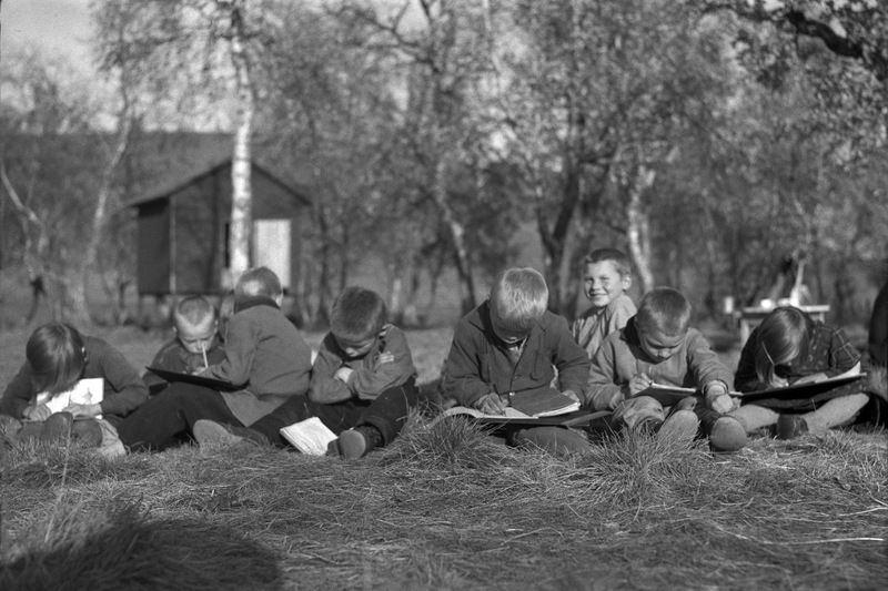 Skolelever sitter i gräset och läser. Vid Nomad...