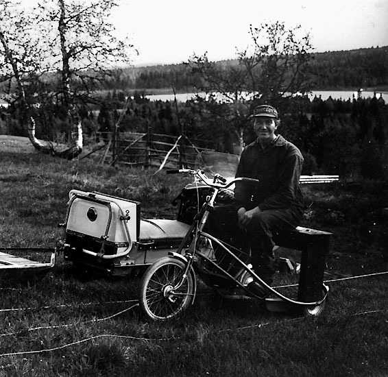 En man på en trehjulig cykel, bredvid en skoter.
