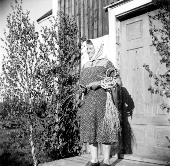 Selma Persson, hon står framför sin stuga med v...