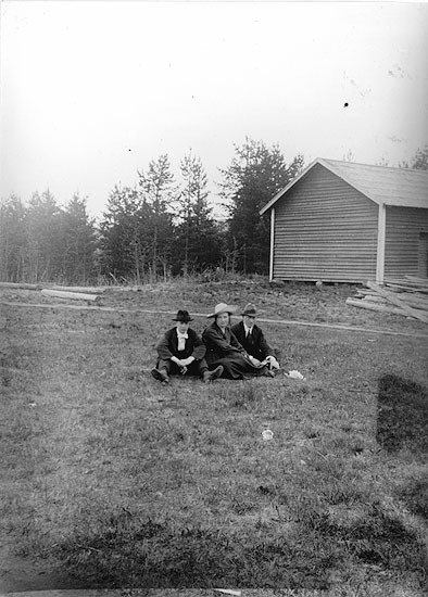 Tre okända ungdomar sittande i gräset.