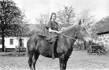 Ung kvinna sittande på häst på gårdsplanen fram...