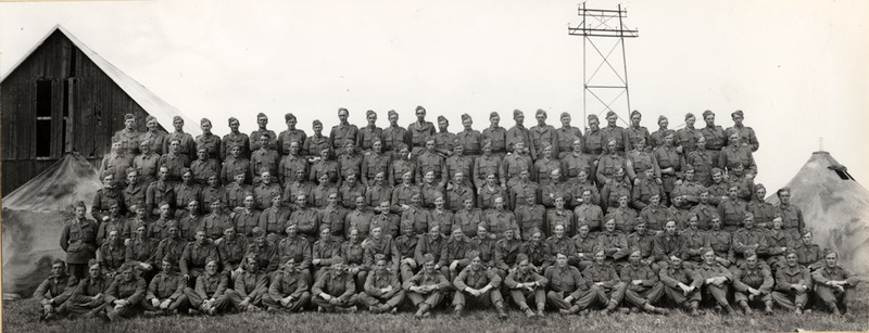 Gruppfoto av befäl och soldater i militärläger. 