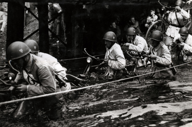 Soldater som drar sina cyklar genom vattendrag ...