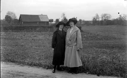 Två kvinnor i hatt på landsbygdsväg.