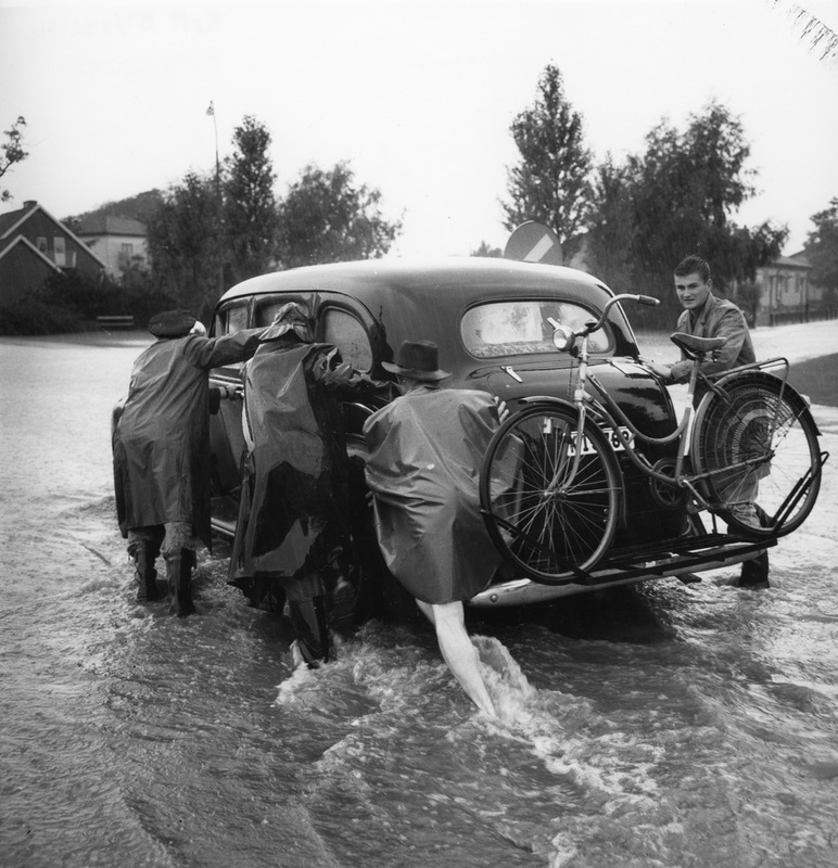Översvämning. Fyra män bärgar en bil ur vattenm...