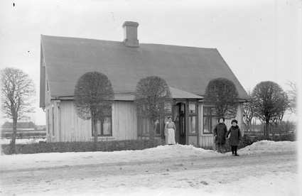 En kvinna och två barn framför hus. Vinter.