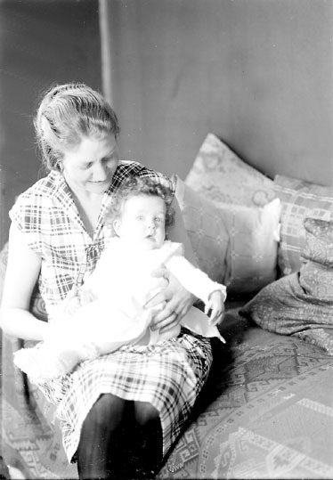 En kvinna och ett spädbarn som sitter på en säng.