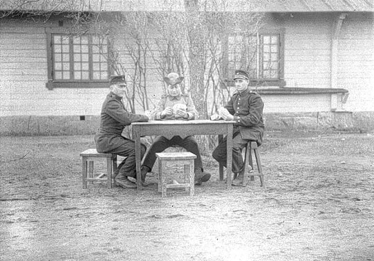 3 kortspelande husarer sitter vid ett bord ute ...