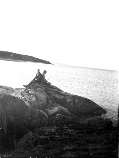 Två män som sitter på en klippa vid havet.