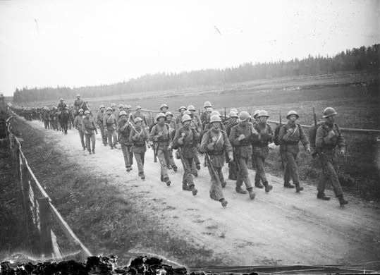 Soldater kommer marscherarande på en landsväg o...