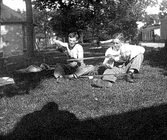 Bilden visar 2 elever som sitter på en gräsmatt...
