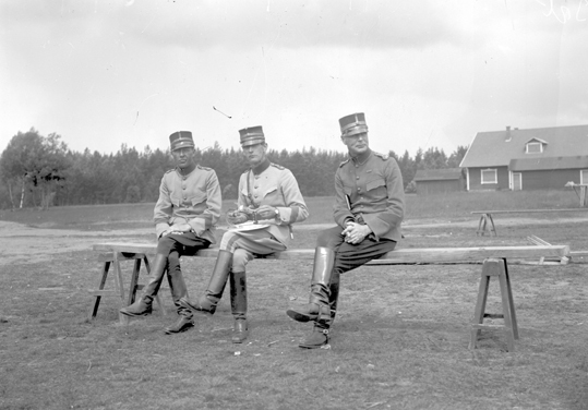 Tre militärer i uniform sitter på en bräda lagd...