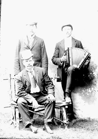 Foto av tre män, en av dem spelar dragspel.