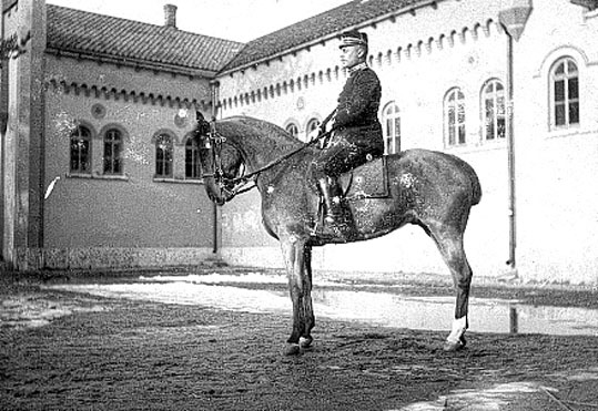 Bilden visar en major till häst framför fästnin...