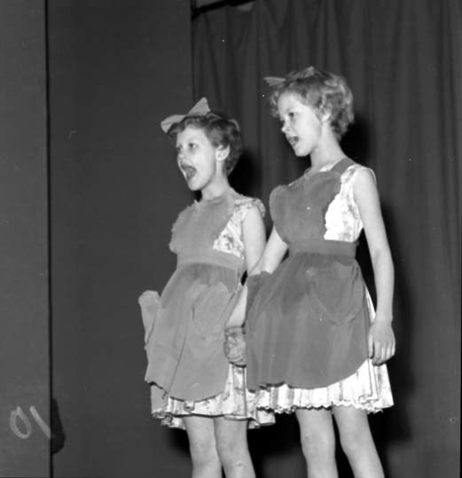 Två glada flickor i klänning och förkläden står...