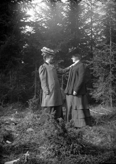 Två promenadklädda kvinnor i skogen. Den ena kv...
