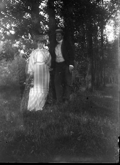 En man och en kvinna står i skogsbrynet. Paret ...